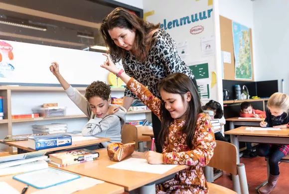 leerkracht helpt leerlingen tijdens schoolopdracht