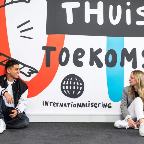 Twee leerlingen praten met elkaar met internationale praatplaat op achtergrond