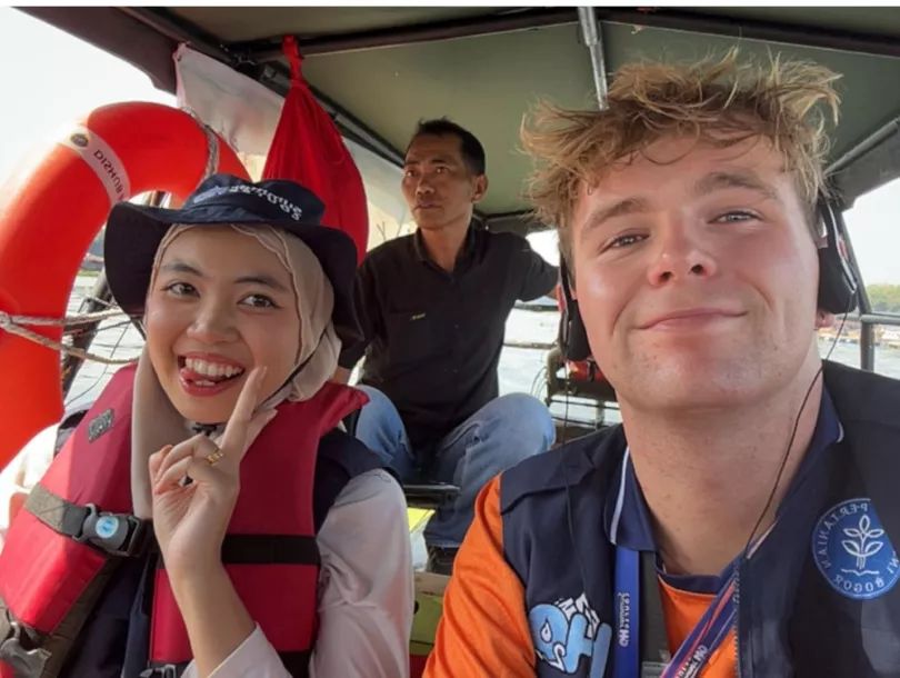 Kai Nijhuis and Muna from Universiti Malaysia Terengganu (UMT), wearing life jackets, take a selfie on a boat while visiting the open-water fish cages at Cirata Reservoir during the H2O Summer Course field excursion.